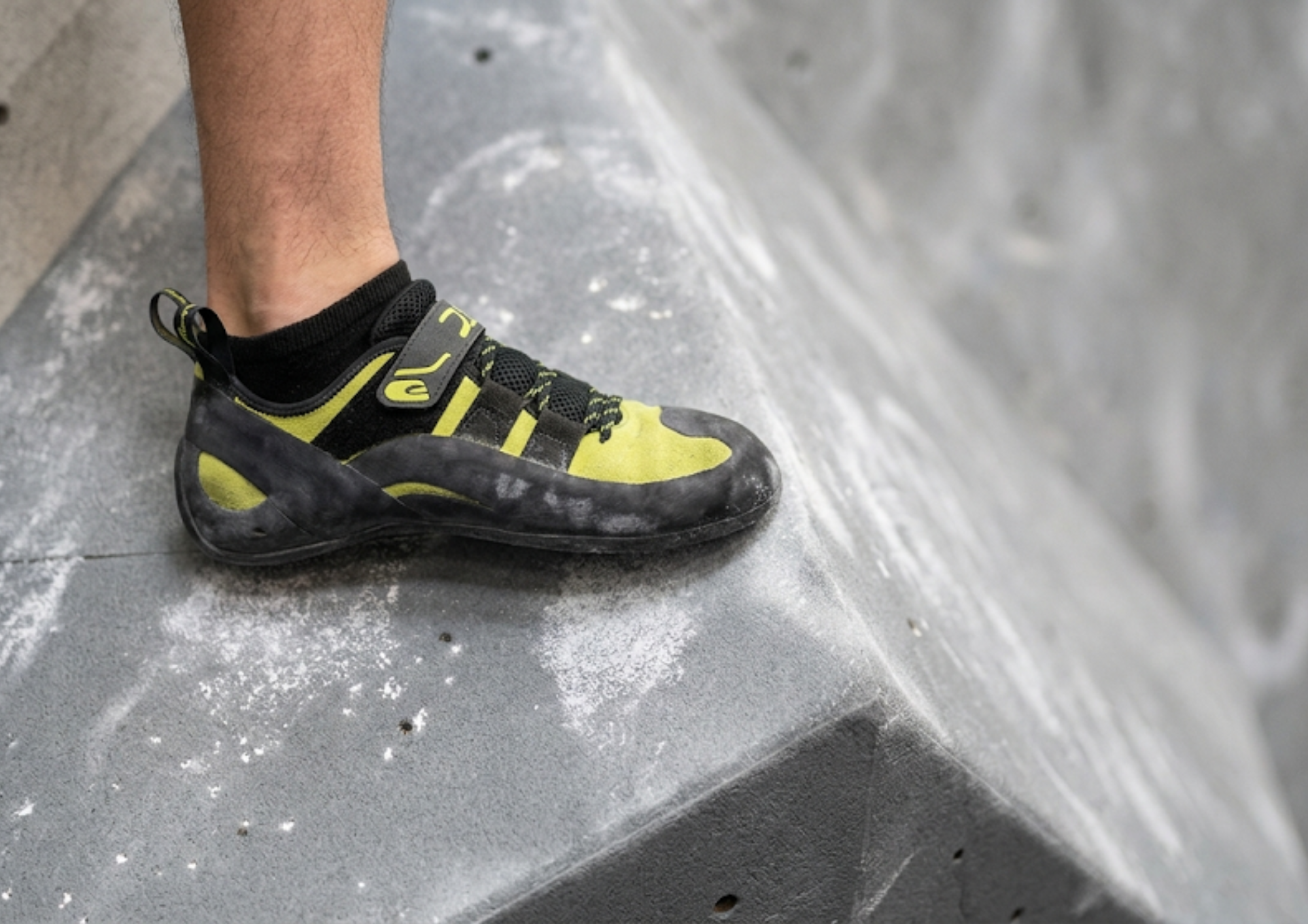 Chausson d'escalade jaune et noir en contact avec un volume gris couvert de magnésie — illustration du coefficient de friction gomme-résine
